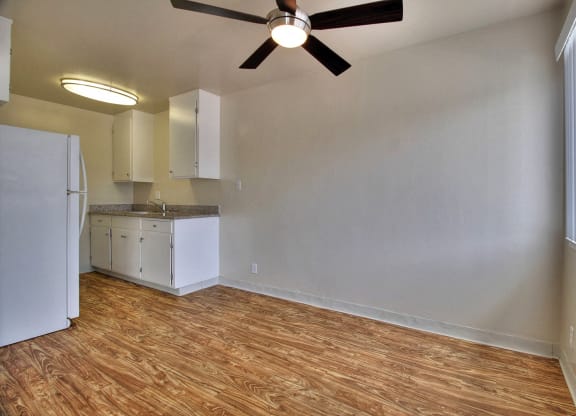 an empty living room with a kitchen and a ceiling fan