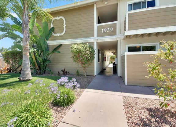 the front of a beige building with a sidewalk and palm tree