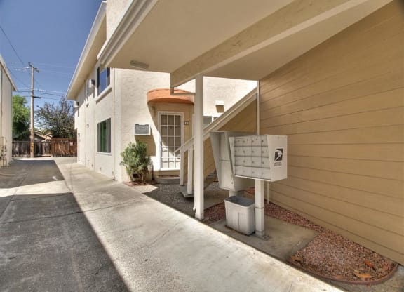 A white mailbox is on the side of a tan building.