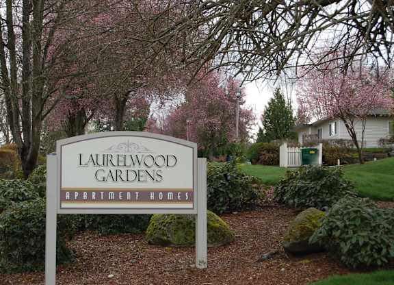 A sign for Laurelwood Gardens Apartment Homes stands in front of a flowering tree.
