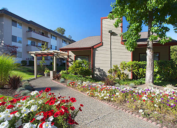 A building with a red roof is surrounded by flowers and trees.