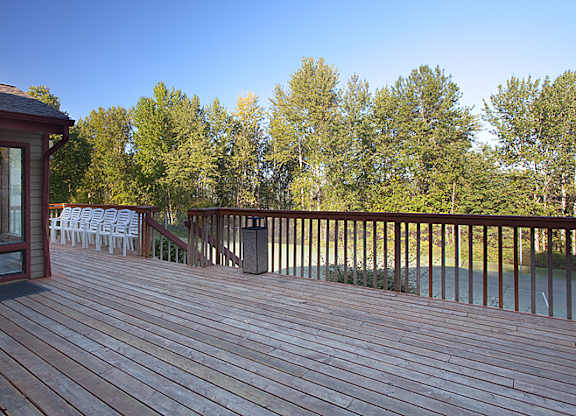 A wooden deck with a red building and trees in the background.