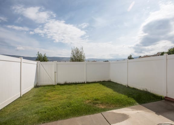 A backyard with a white fence and a concrete patio.