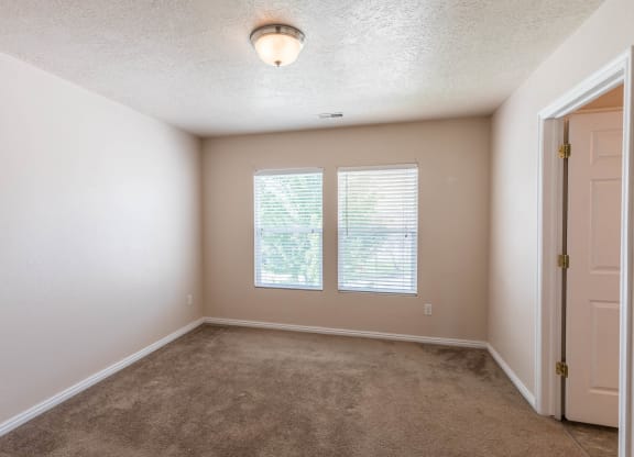 A room with a carpeted floor, a ceiling light, and a door.