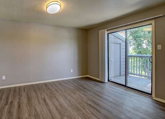 A room with wooden flooring and a sliding glass door leading outside.