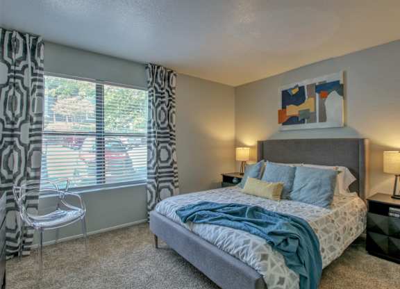 A bedroom with a bed, chair, and window with curtains.