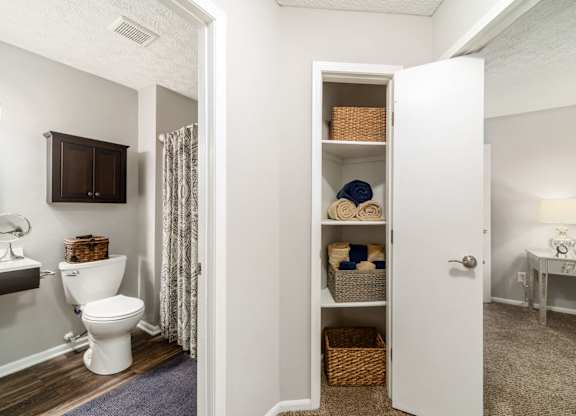 A white bathroom with a toilet, a cabinet, a towel, and a basket.