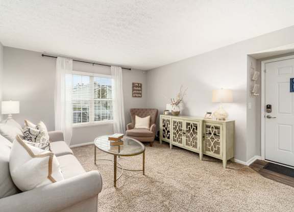 A living room with a white couch, a coffee table, and a window with curtains.