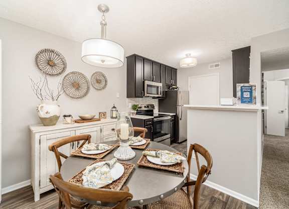 A dining table with chairs and a decorative wall hanging above it.