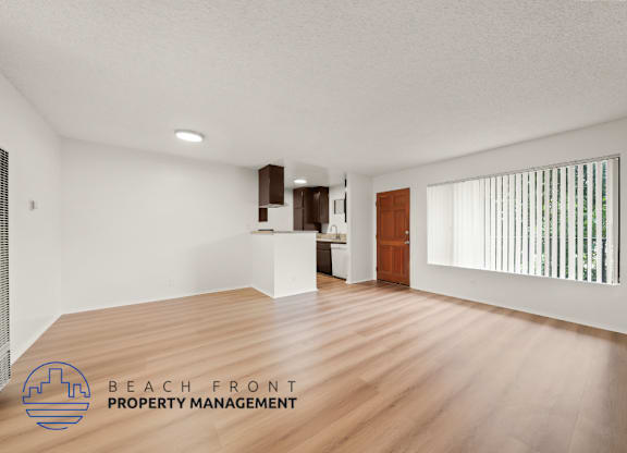 A spacious room with wooden flooring and a logo for Beach Front Property Management in the corner.