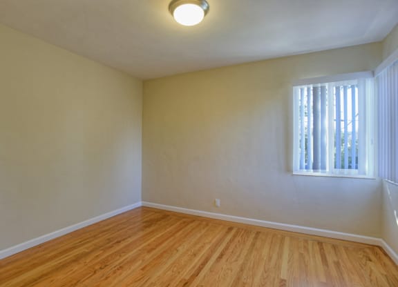 A room with wooden floors and a window with blinds.