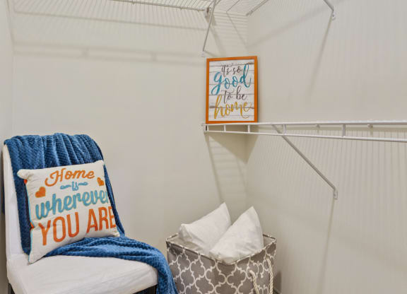a walk in closet with a chair and a basket on the floor