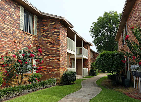 a walkway in front of a brick building with red flowers