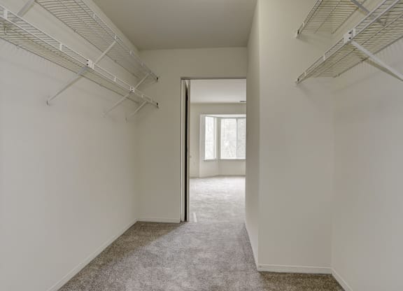 a walk in closet in a bedroom with white walls and a door to a room