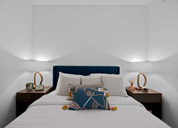 A bed with a blue headboard and a white comforter with a pillow and a teddy bear on it.