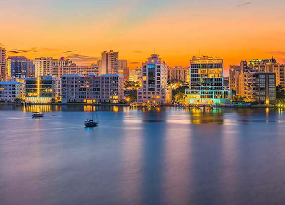 A city skyline at dusk with buildings reflecting on the water.