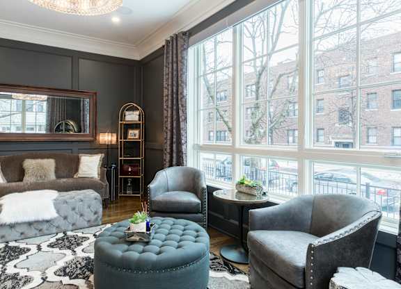 A living room with a grey couch, a grey armchair, a grey ottoman, and a black and white rug.