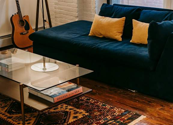 A living room with a blue couch and a guitar hanging on the wall.