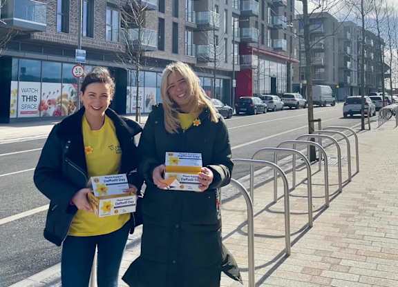Two women in yellow shirts holding boxes on a city street. at Cherrywood Apartments, D18 VY3V