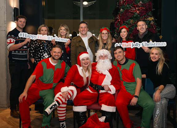 A group of people dressed as Santa and elves are posing for a photo in front of a Christmas tree. at Cherrywood Apartments, D18 VY3V