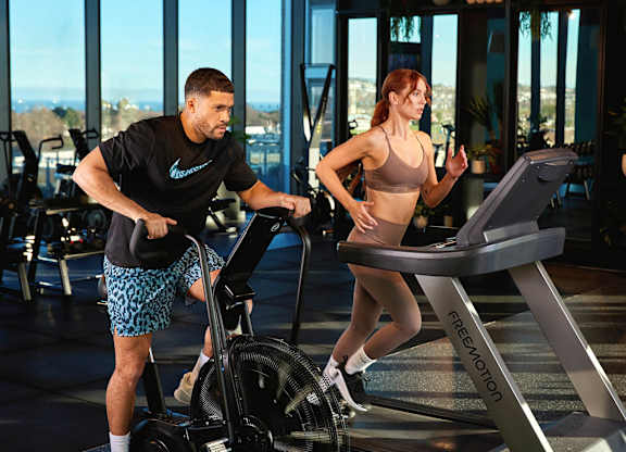 A man and a woman are exercising on elliptical machines in a gym at Cherrywood Apartments, D18 VY3V