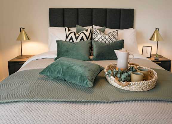 A bed with a grey comforter and a basket on top of it at Cherrywood Apartments, D18 VY3V