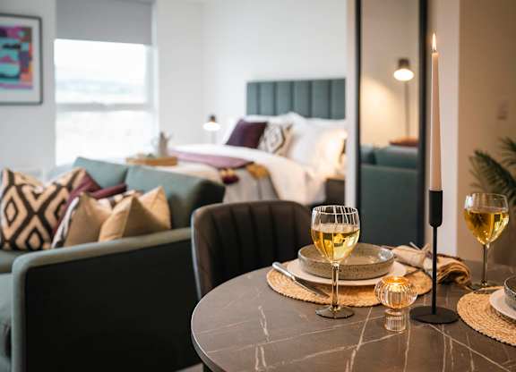 A table with two glasses of white wine and plates is set for two in a modern living room at Cherrywood Apartments, D18 VY3V