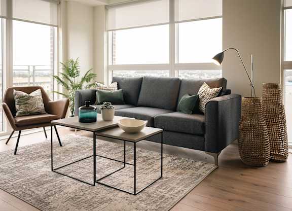 A living room with a grey couch, a brown chair, a glass table with a plant on it, and a large window with a view of the city at Cherrywood Apartments, D18 VY3V, DUBLIN 18