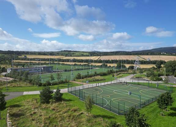 A basketball court surrounded by a green fence with a cloudy blue sky in the background at Cherrywood Apartments, D18 VY3V