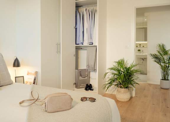 A bedroom with a bed, a pink purse, sunglasses, and a plant at Cherrywood Apartments, D18 VY3V