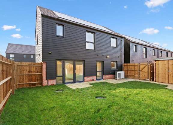 A modern house with a grey exterior and a green lawn in front at The Woodlands Apartments, Milton Keynes