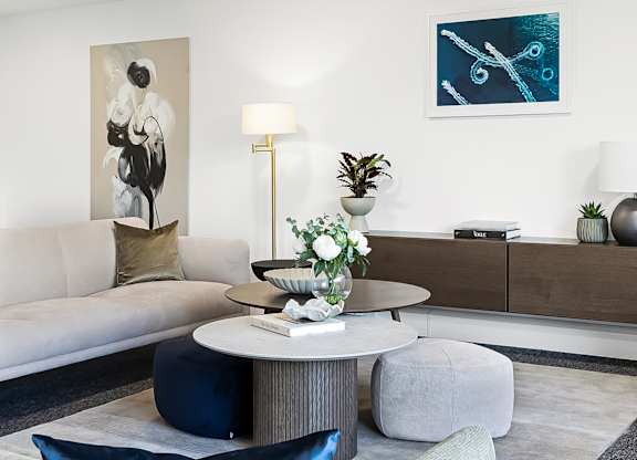 A living room with a grey couch, a round table with a vase of flowers, and a painting on the wall.