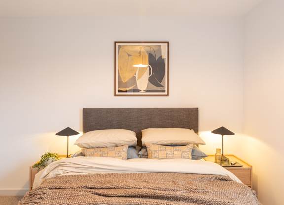 A bed with a grey headboard and a brown blanket with a framed picture above it.