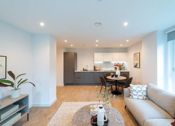 A modern living room with a grey couch, a coffee table, and a dining table set up.