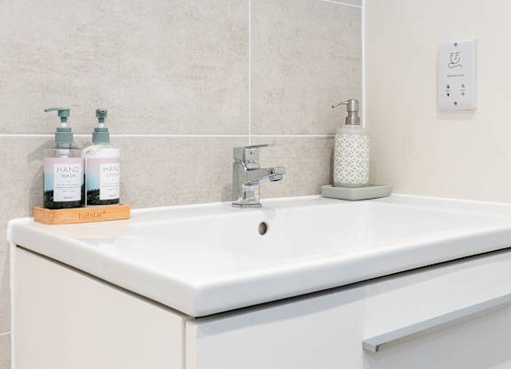 A white sink with a soap dispenser and two bottles of hand soap on a wooden stand.