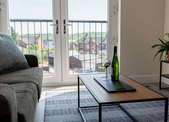 A living room with a grey couch and a green bottle on a table.