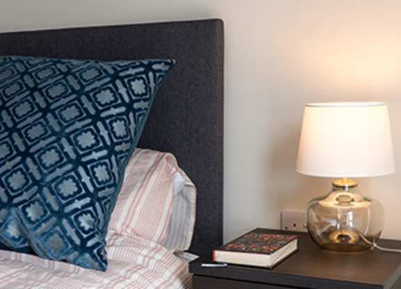 A bed with a blue pillow and a lamp on a nightstand.