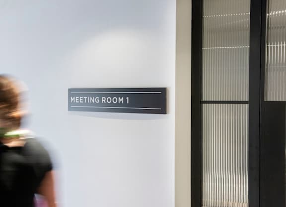 Woman walking past sign meeting room 1 at The Lark, London, SW11 7EA