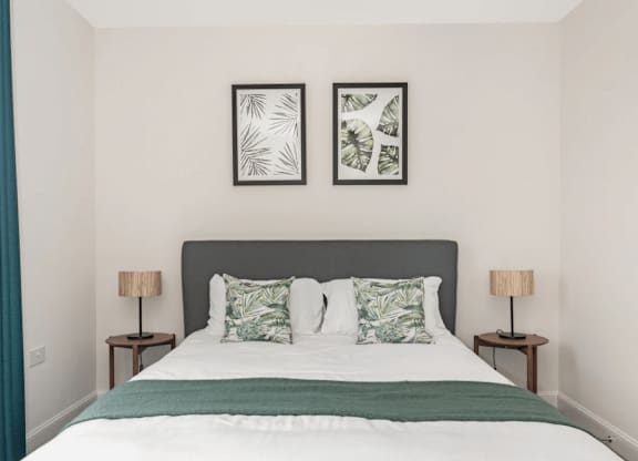 A bed with a white comforter and two green throw pillows at Origins Apartments, Cambridge