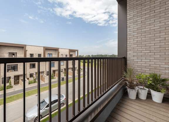 A balcony with a black railing and potted plants overlooks a street with cars and houses at Origins Apartments, Cambridge, CB3 0UX