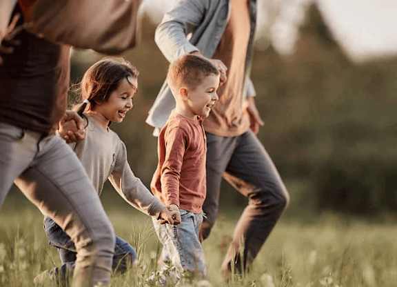 A group of people, including children, are playing in a grassy field at Origins Apartments, Cambridge, CB3 0UX