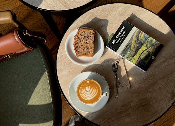A table with a cup of coffee, a book, and a piece of cake on it.