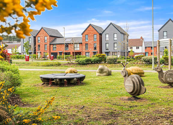 A park with sculptures of snails and a bench in front of apartment buildings.