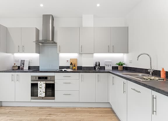 A modern kitchen with white cabinets and a stainless steel range hood at The Woodlands Apartments, Milton Keynes, MK5 6GS