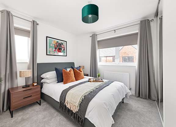 A bedroom with a large bed, a nightstand with a lamp, and a framed picture on the wall at The Woodlands Apartments, Milton Keynes