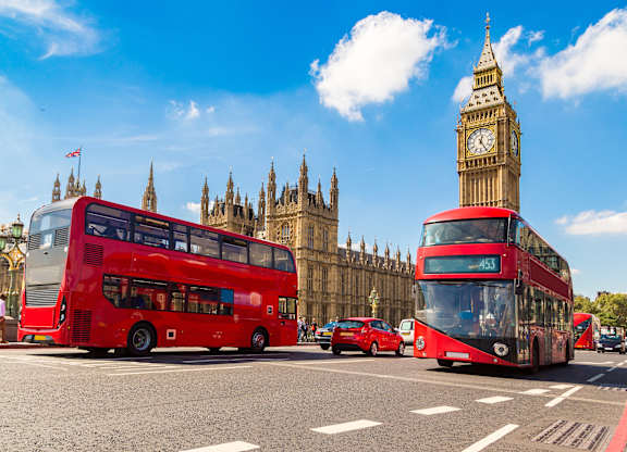 Two red double-decker buses are driving in front of the Big Ben and the Houses of Parliament.