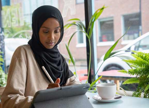 A woman in a hijab is writing on a tablet.