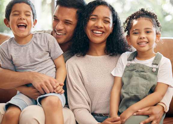 A family of three is sitting closely together on a couch.
