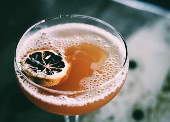 A glass of a bubbly drink with a slice of citrus garnish.