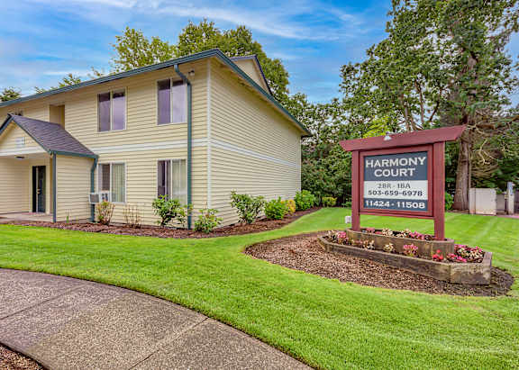 A beige house with a red sign that says Harmony Court in front of it.